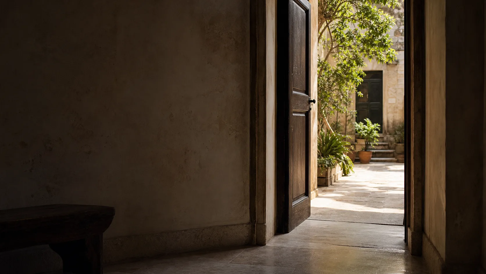 An open timber doorway leading from a quiet stone interior to a sunlit courtyard